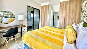 A hotel room with a bed, a desk, a chair, a ceiling fan, and a door leading to another room. - Romsey Holiday Breeze (Durban North)