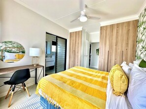 Een hotelkamer met een bed, een bureau, een stoel, een plafondventilator en een deur die naar een andere kamer leidt.