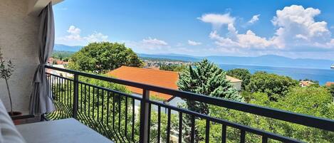 A balcony with a view of a coastal landscape, including trees and buildings.