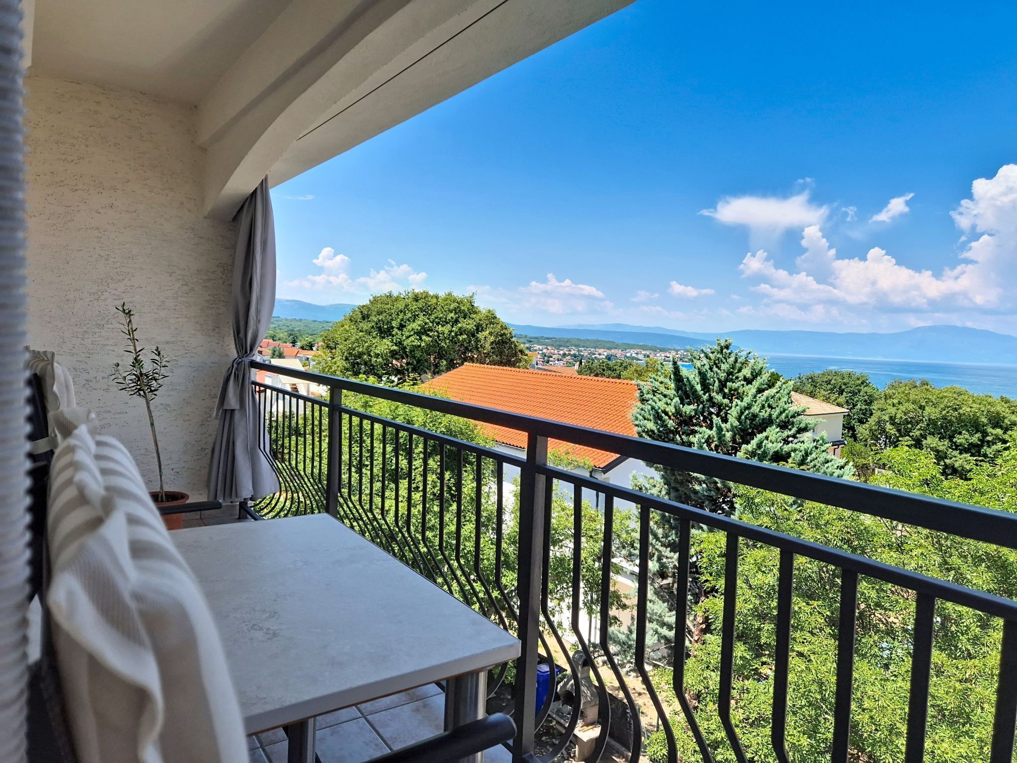 Ein Balkon mit Blick auf eine Küstenlandschaft, einschließlich Häuser und Bäume.
