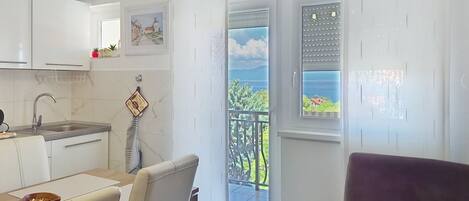 A modern kitchen with white cabinets, a dining area with a table and chairs, and a balcony with a view of the sea.