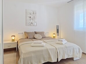 A modern bedroom with a large bed, two bedside tables, a wall-mounted artwork, and a window with blinds. - Apartment Emma by Interhome (Krk/Malinska)