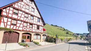 Ein traditionelles Fachwerkhäus mit einer großen Holztür, einer Steinmauer und einem Weinberg im Hintergrund.