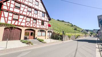 Ein traditionelles Fachwerkhäus mit einer großen Holztür, einer Steinmauer und einem Weinberg im Hintergrund.