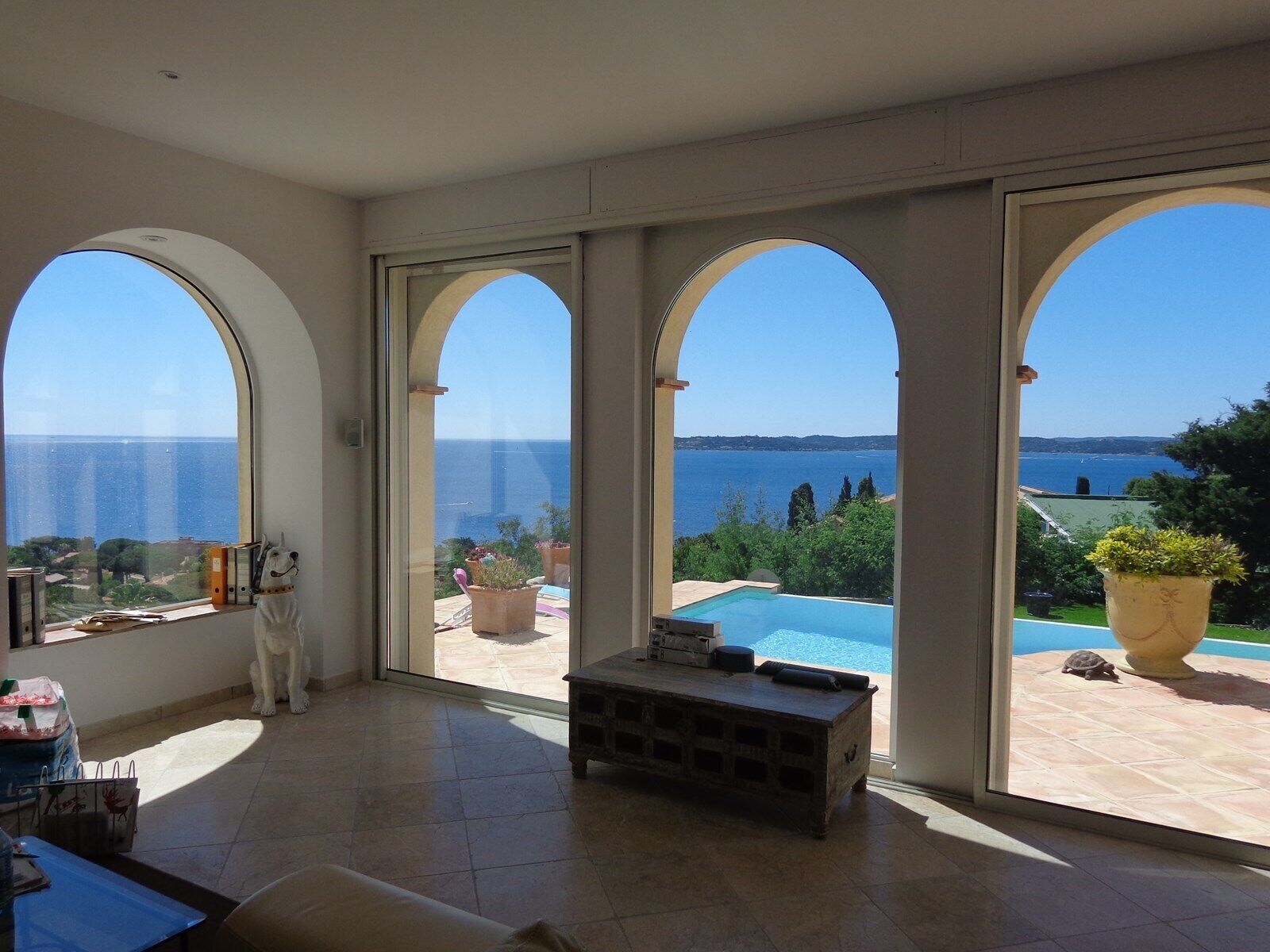 Une pièce spacieuse dotée de grandes fenêtres en arc de cercle, d’une piscine et offrant une vue sur la mer.