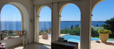 A spacious room with large arched windows, a pool, and a view of the sea.