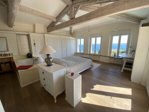 Ein Schlafzimmer mit Bett, Schreibtisch, Kommode und Meerblick.