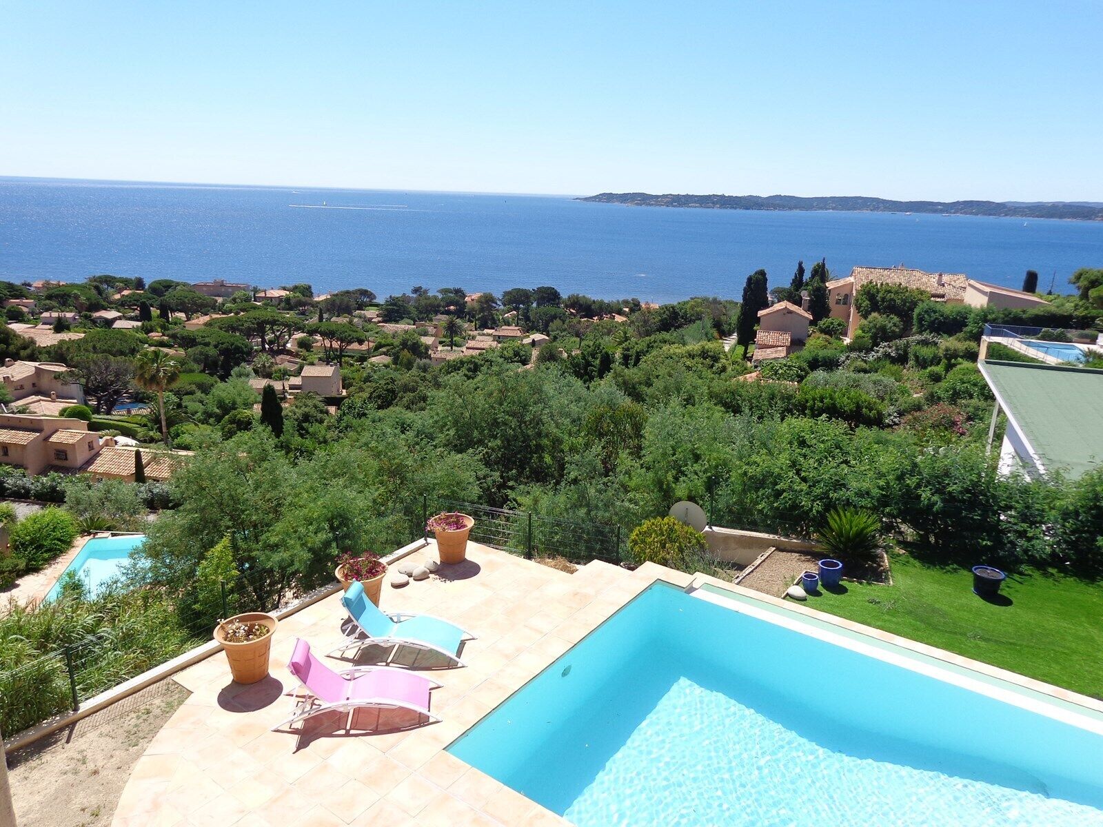 Ein Pool mit Liegestühlen, Blick aufs Meer und umliegende Grünflächen.