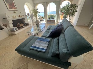 Ein Wohnzimmer mit einem grünen Sofa, einem Kamin und Blick aufs Meer.
