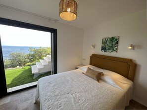 Ein Schlafzimmer mit großem Fenster, einem Bett, einem Kopfteil und einer Pendelleuchte.