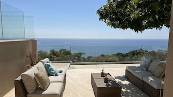 Uma varanda com dois sofás de vime, uma mesa pequena e vista para o mar.