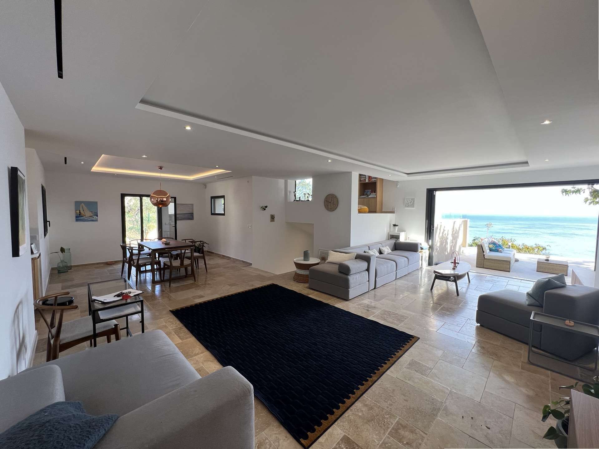 Uma sala ampla com uma mesa de jantar, sofás e uma grande janela com vista para o mar.