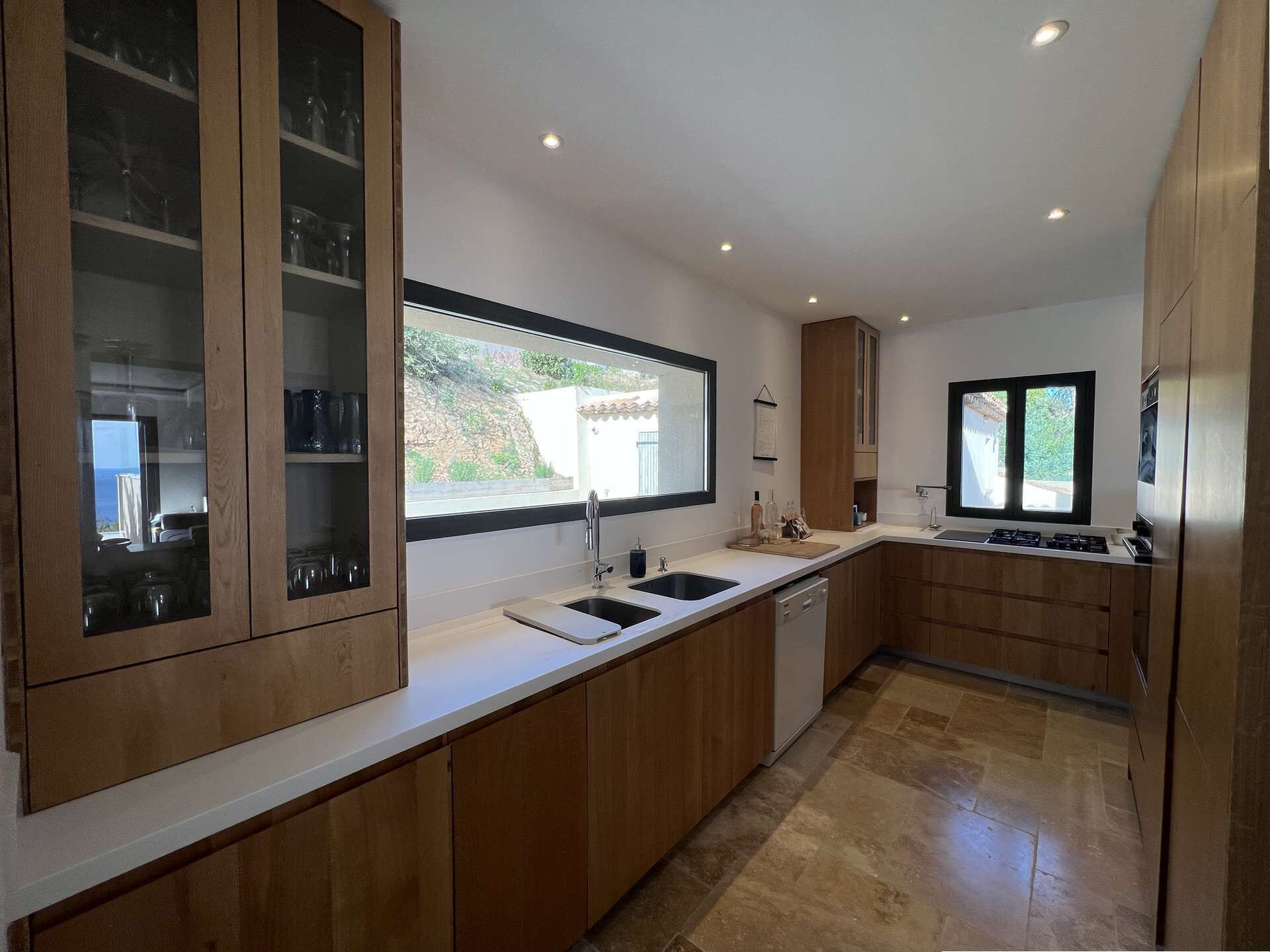 Une cuisine moderne avec des meubles en bois, une grande fenêtre et un lave-vaisselle encastré.