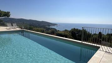 Piscina límpida com vista para o mar e colinas.