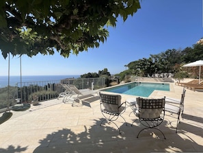 Ein Poolbereich mit Meerblick, zwei Liegestühle und eine kleine Terrasse.