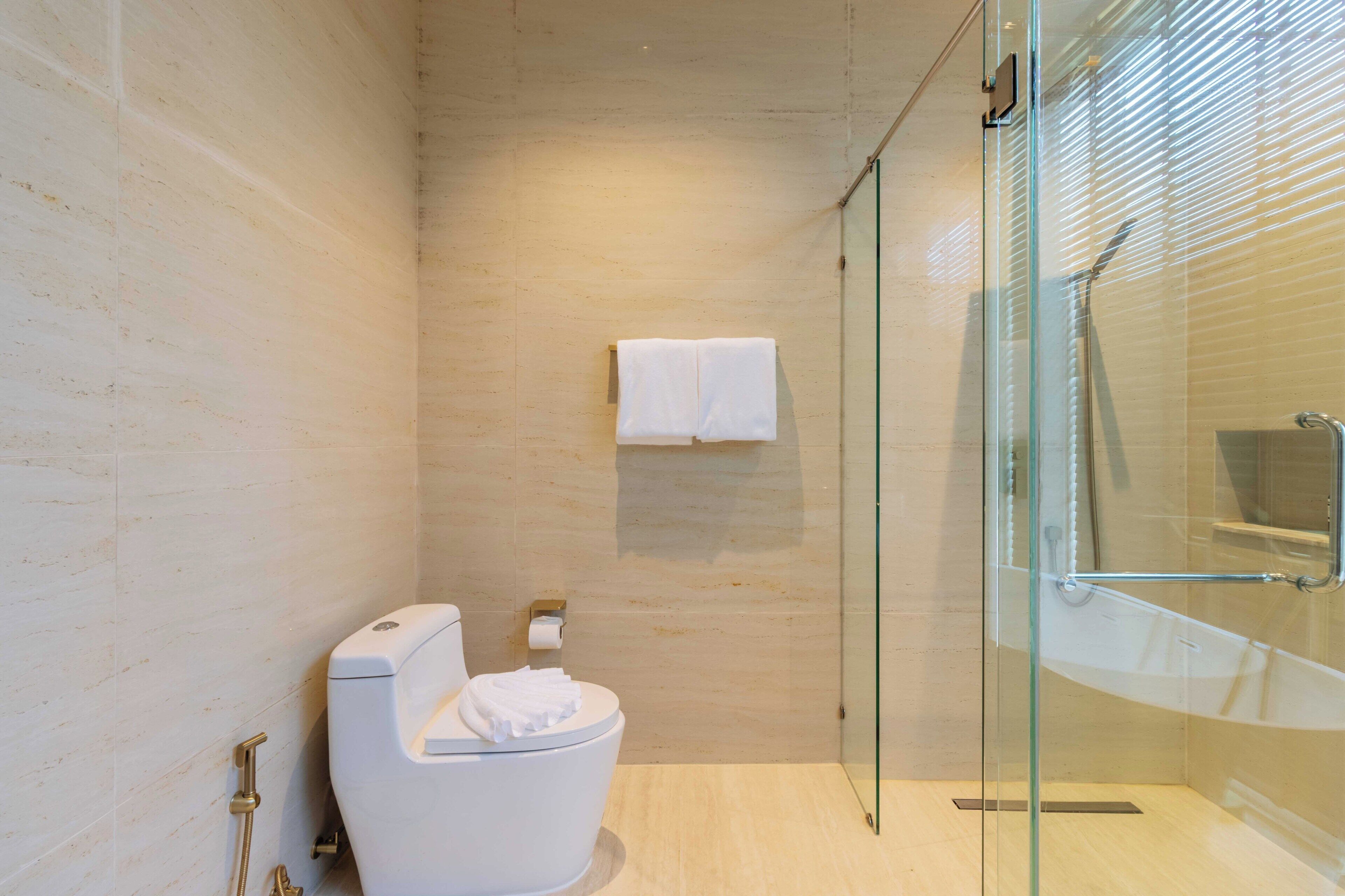 A modern bathroom with a glass-enclosed shower, a toilet, and a towel rack.