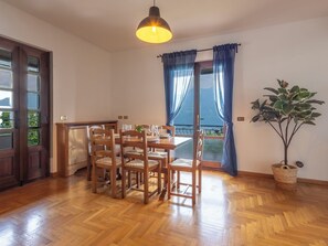 A dining area with a wooden table and chairs, a hanging light fixture, a potted plant, and a view through a door. - Ortigara Terrace View by Interhome (Lovere)