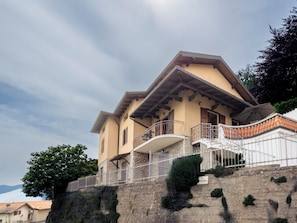 Um edifício de dois andares com varanda, parede de pedra e uma placa indicando uma Via.