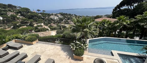 Ett område vid poolen med solstolar, ett bubbelbad och utsikt över havet och kullarna.
