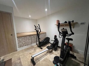 Ein Heimfitnessraum mit Trainingsgeräten, darunter ein Ergometer, ein Crosstrainer und eine Gewichtbank.