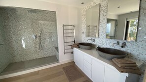 Ein modernes Badezimmer mit Duschkabine aus Glas, einem großen Waschbecken und einer gefliesten Rückwand.