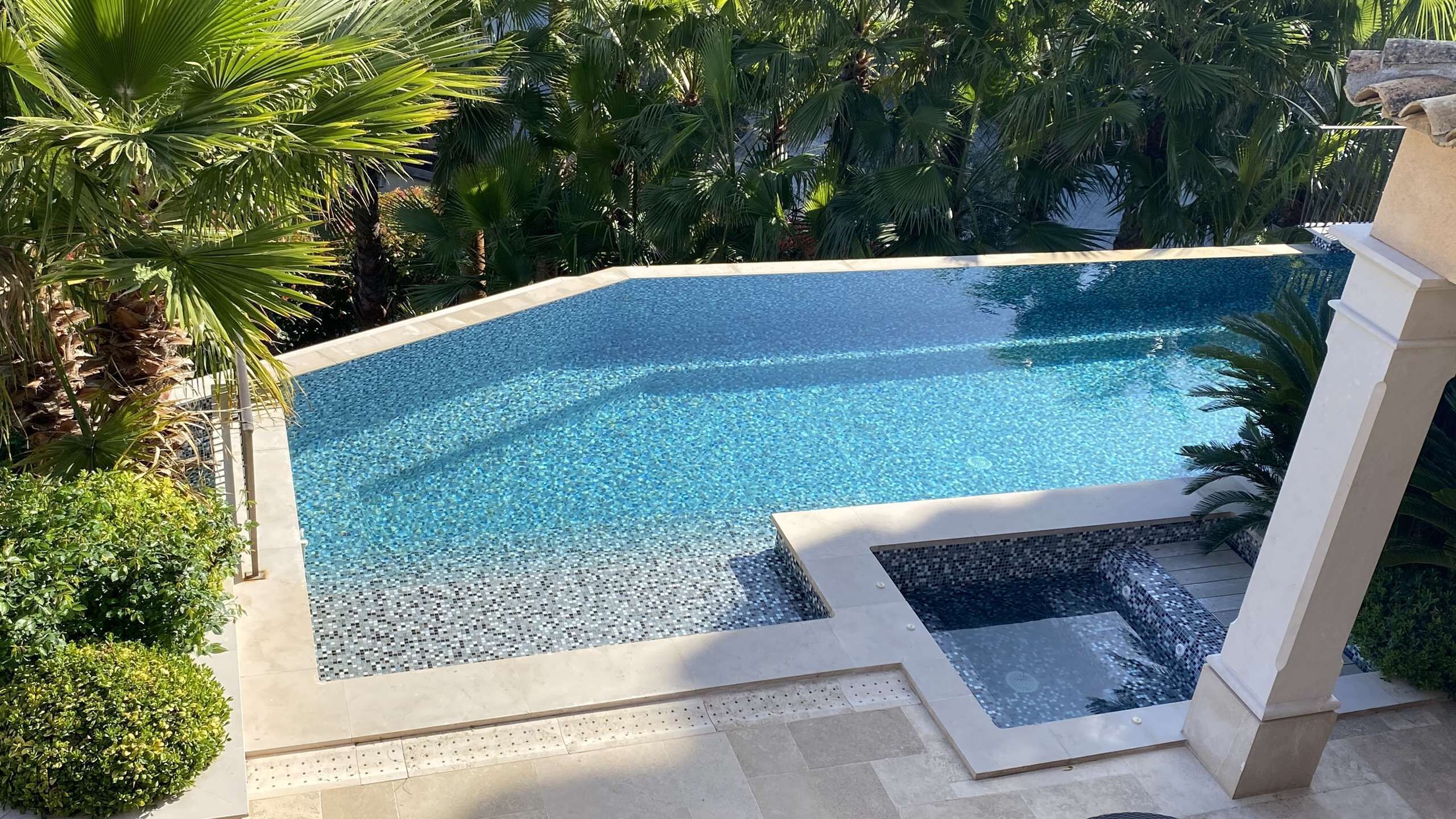 Una piscina infinita de color azul intenso, con un borde de baldosas, rodeada de exuberante vegetación y palmeras.