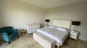 Ein Schlafzimmer mit einem Bett, einem Nachttisch, einem Beistelltisch, einem Sessel und einer Lampe.