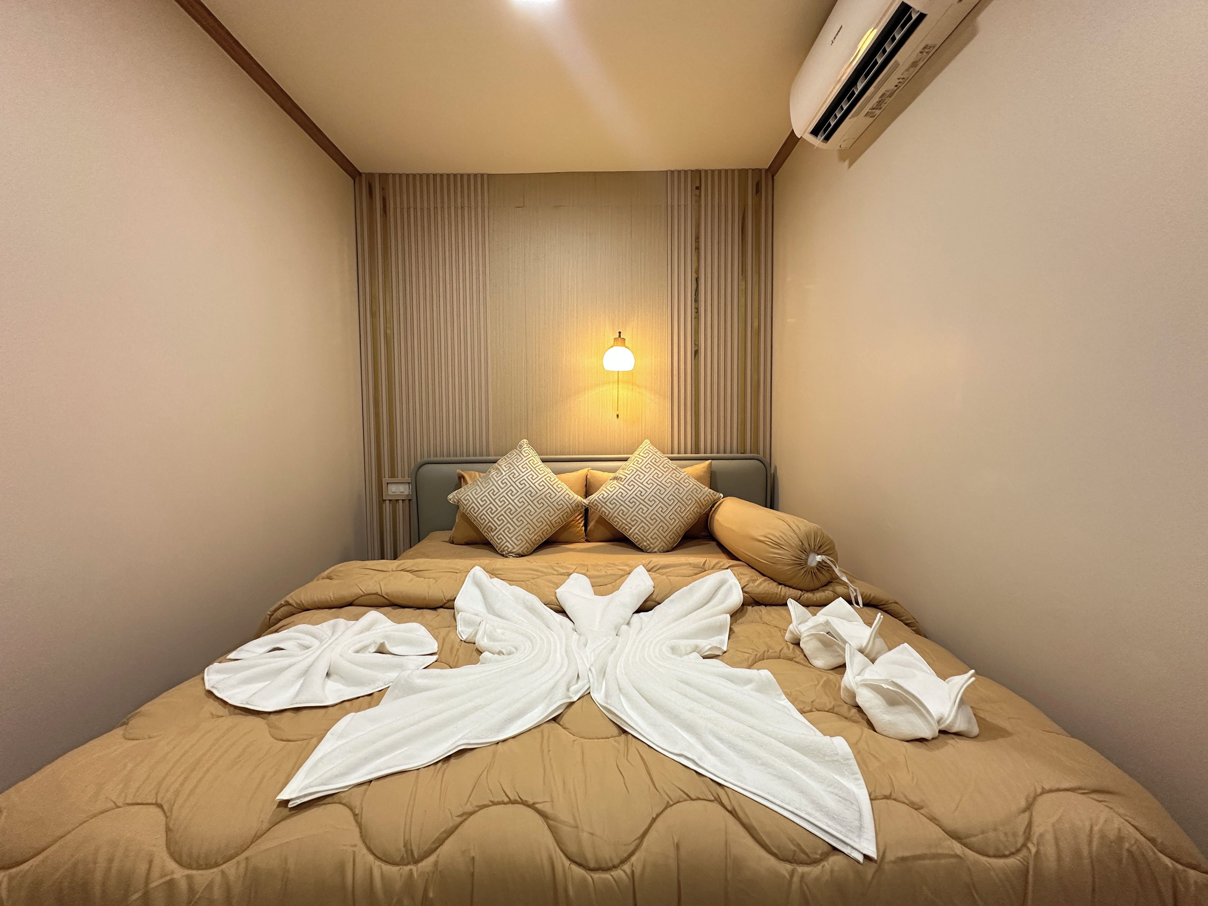 A hotel room with a bed, a wall-mounted air conditioner, and a bedside lamp.