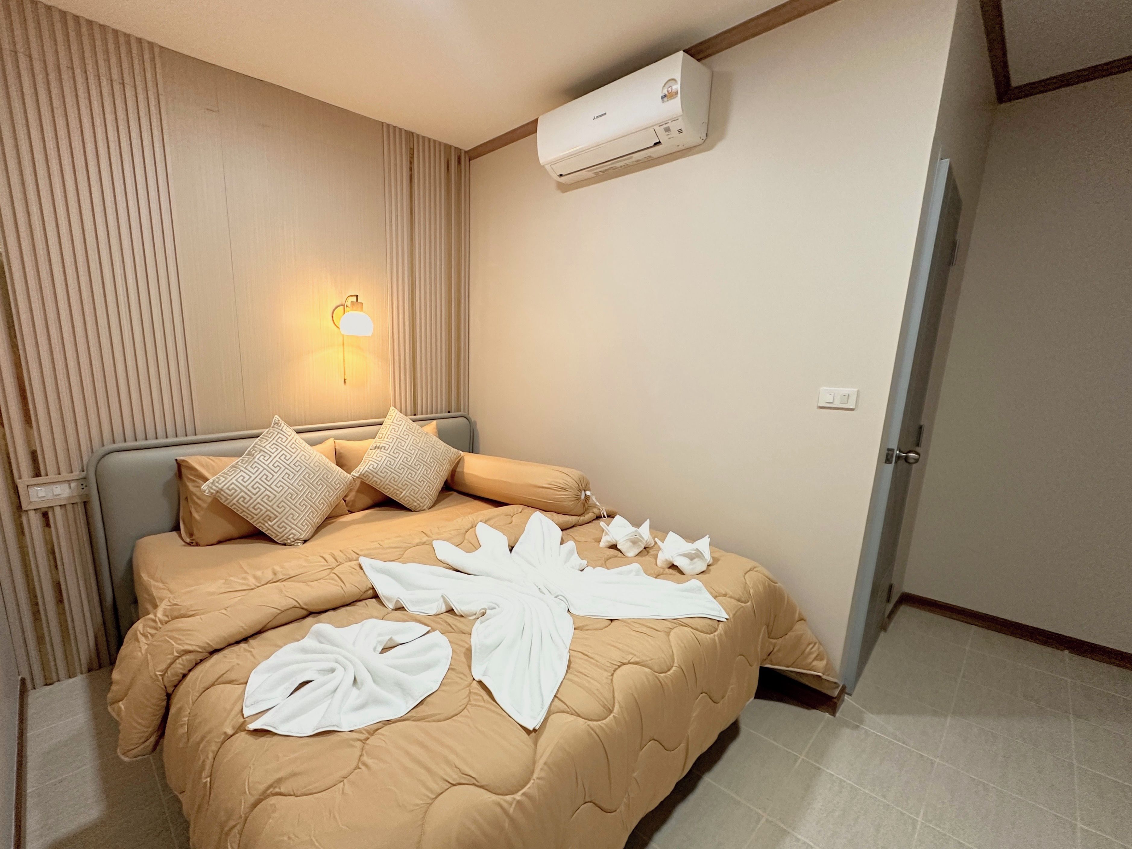 Una habitación de hotel con una cama, aire acondicionado de pared, una lámpara de noche y una puerta.
