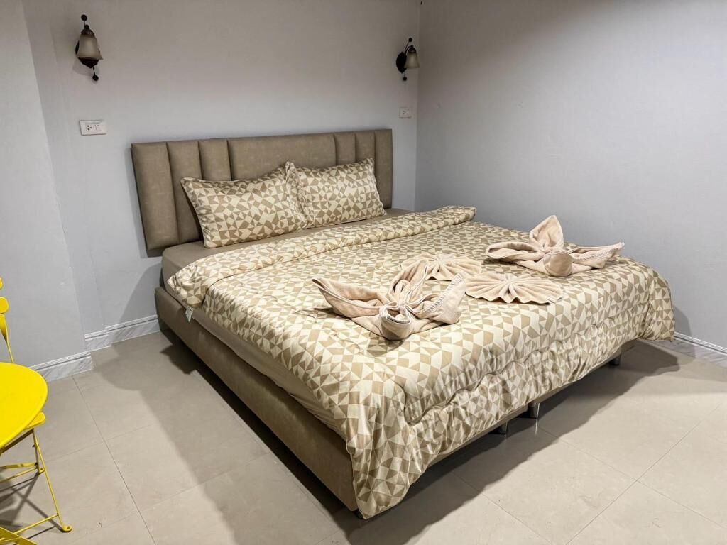A bed with a geometric patterned bedspread and pillows, a bedside lamp, and a yellow chair.