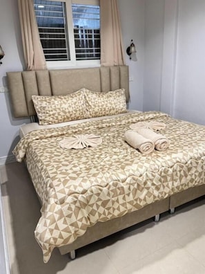A bed with a geometric patterned bedspread, a headboard, and a window with curtains. - Miley Phi Phi Guesthouse (Ko Phi Phi)