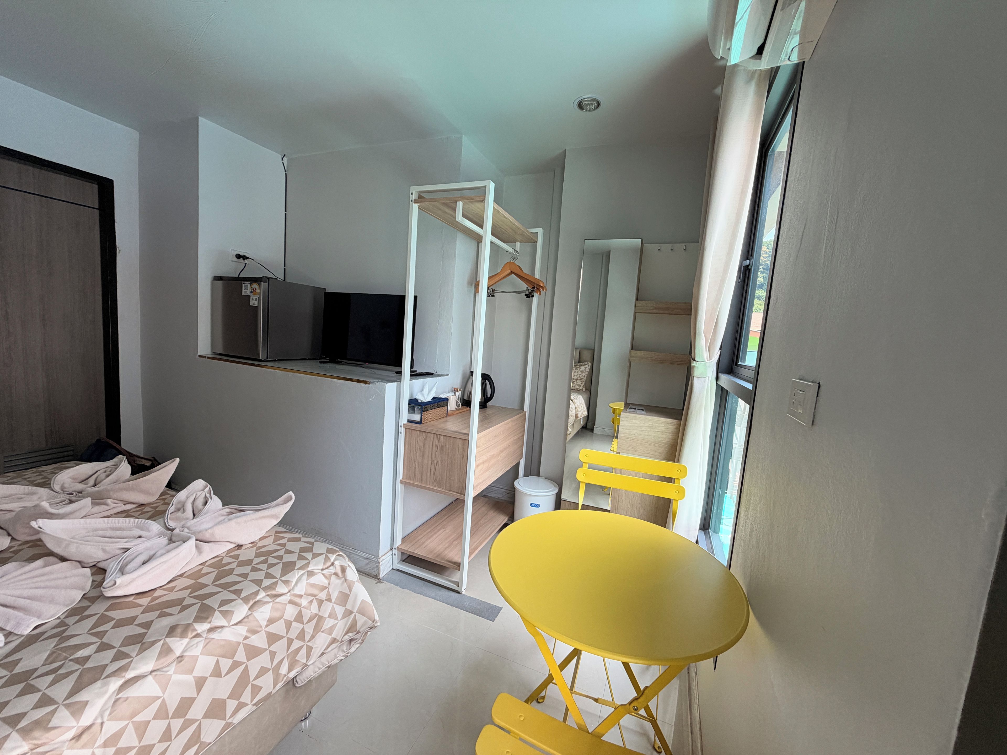 Une chambre d’hôtel de taille réduite, comprenant un lit, une petite table, une chaise, un coin cuisine et une salle de bain.