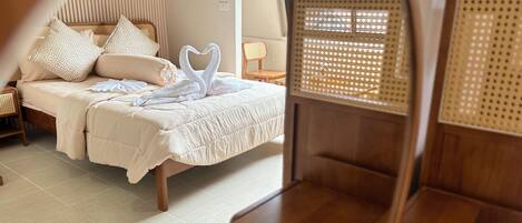 A room with a bed, a wooden bench, and a window with a woven blind.
