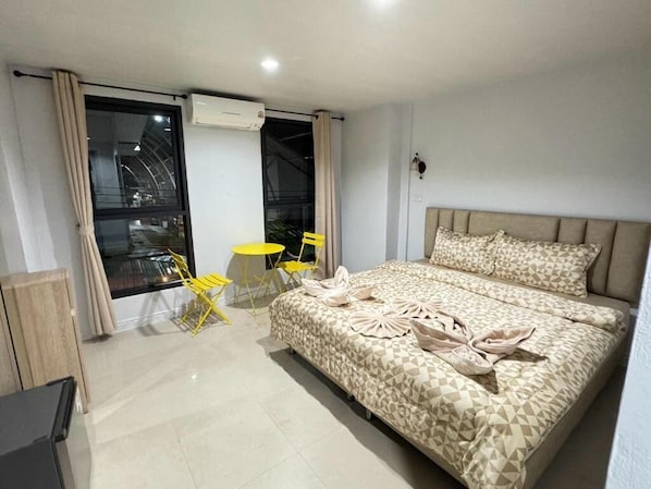 A hotel room with a bed, a small table, two chairs, an air conditioning unit, and a view through a window. - Miley Phi Phi Guesthouse (Ko Phi Phi)