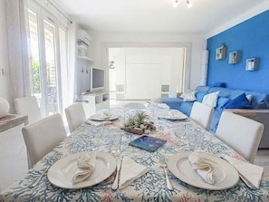 A dining area with a table set for four, a blue wall, and a sofa in the background. - El Rayo del Sol by Interhome (Six Fours)