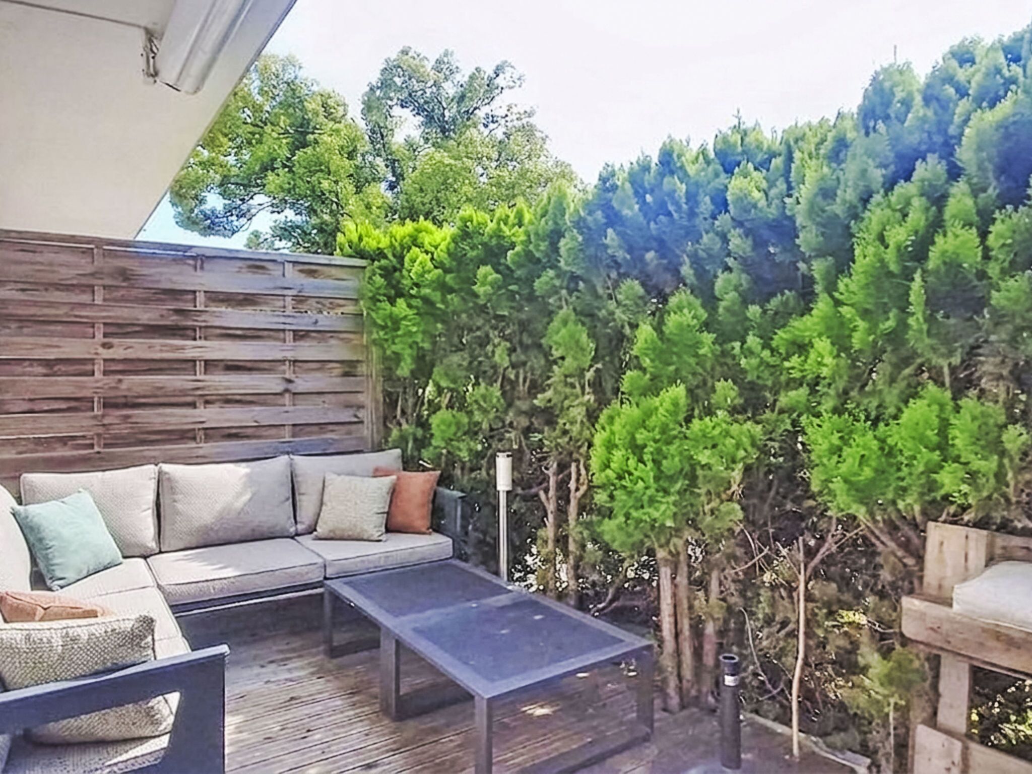 Un patio al aire libre con una terraza de madera, un sofá con cojines y una mesa.