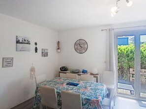 A dining area with a table, chairs, a clock, and a view of greenery outside. - El Rayo del Sol by Interhome (Six Fours)