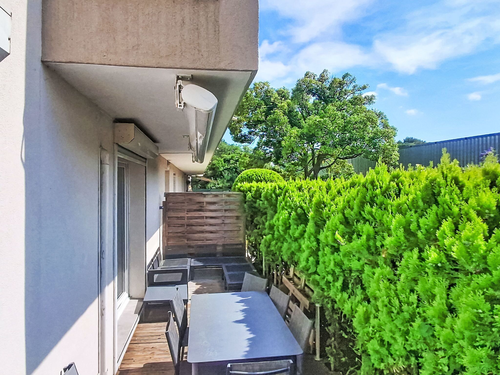 Une terrasse avec une table et des chaises, une clôture en bois et une haie.