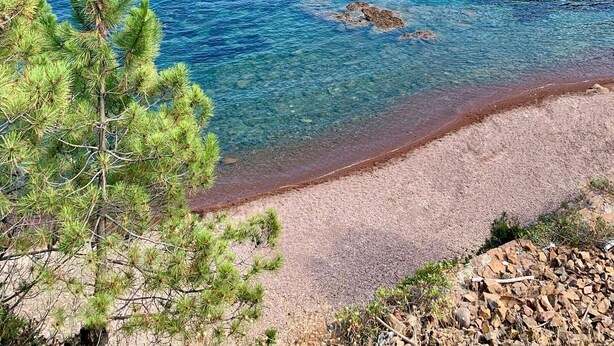 A coastal landscape with clear blue water, rocky outcrops, and a building on a hill. - SAINT-RAPHAËL CITY CENTER – BEACH WITHIN WALKING DISTANCE – COMFORTABLE 1-BEDROOM APARTMENT (ST RAPHAEL)