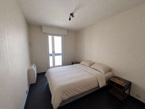 Ein Schlafzimmer mit einem Bett, einem Nachttisch, einem kleinen Tisch, einer Deckenleuchte und einer Schiebetür zum Balkon.