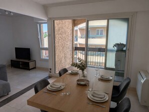 Ein Essbereich mit einem Holztisch, gedeckt für vier Personen, einem Fernseher in der Ecke und Blick auf einen Balkon mit Geländer.