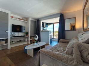 Un salon moderne avec un canapé, un téléviseur à écran plat, une table basse et un balcon offrant une vue agréable.