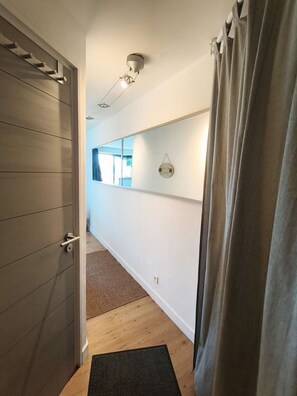 Ein Korridor mit einer Holztür, einer schwarzen Fußmatte, einer Wandleuchte und einem Fenster.