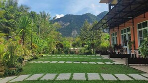 A courtyard with a paved walkway, lush greenery, and a mountain backdrop. - Khao Sok Country Resort (Phanom)