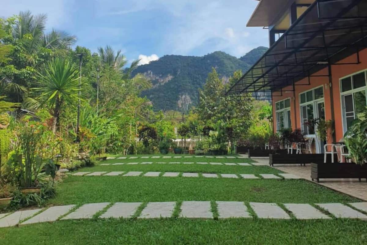 Un patio con un camino empedrado, abundante vegetación y montañas al fondo.
