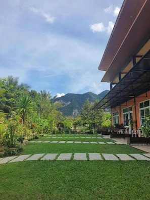 A courtyard with a paved walkway, lush greenery, and a mountain backdrop. - Khao Sok Country Resort (Phanom)