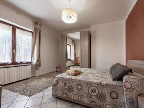 Ein Schlafzimmer mit Bett, Nachttisch, Spiegel, Fenster mit Vorhängen und Heizkörper.