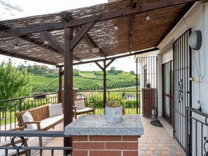 A balcony with a wooden pergola, a stone table, and a seating area with a bench and chairs. - Bellavista by Interhome (Neive)