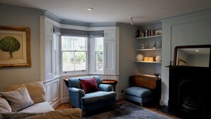Ein Wohnzimmer mit blauem Sessel, beiger Couch, Kamin und Bücherregal.