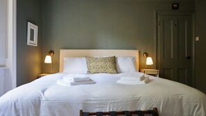 Ein ordentlich gemachtes Bett mit weißen Leinentüchern und einem Kopfkissen, zwei Nachttische mit Lampen und eine Tür rechts.